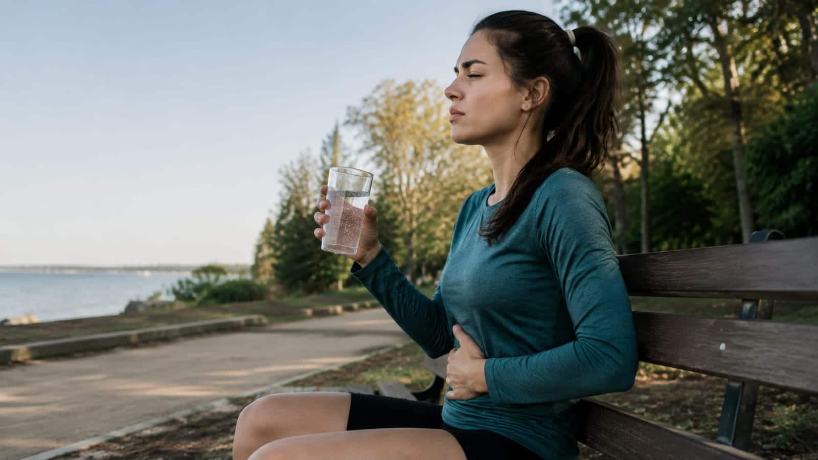 Runner pausing with sparkling water and hand resting lightly over a bloated stomach